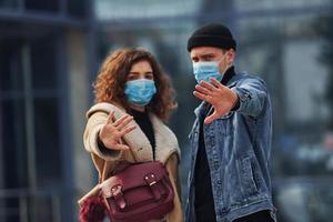Couple in protective masks have a walk outdoors in the city near business building at quarantine time. Conception of coronavirus photo