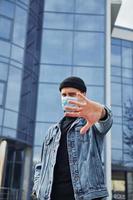 Portrait of young guy in protective mask that standing outdoors near business building at quarantine time. Conception of coronavirus photo