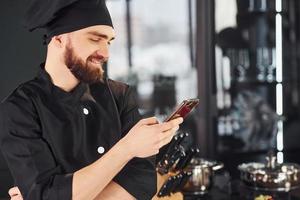 Professional young chef cook in uniform standing with phone on the kitchen photo