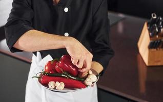 With vegetables. Professional young chef cook in uniform working on the kitchen photo