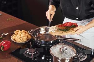 Using equipment. Professional young chef cook in uniform working on the kitchen with vegetables photo