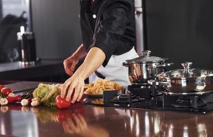 With vegetables. Professional young chef cook in uniform working on the kitchen photo