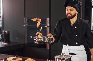 Professional young chef cook in uniform frying food on the kitchen photo