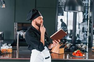 Professional young chef cook in uniform standing with notepad on the kitchen photo