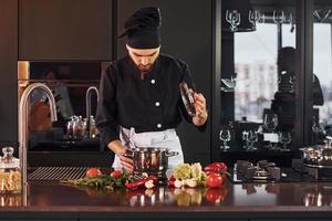 utilizando equipo. Cocinero profesional joven en uniforme trabajando en la cocina con verduras foto