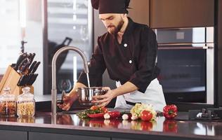 Using equipment. Professional young chef cook in uniform working on the kitchen with vegetables photo