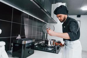 Cocinero profesional joven en uniforme de pie en la cocina foto