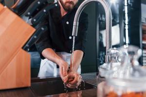 Cocinero profesional joven en uniforme lavándose las manos en la cocina foto