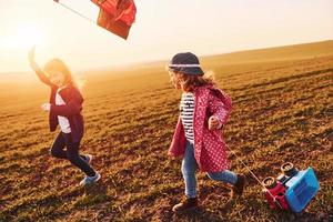 dos amigas se divierten juntas con cometas y autos de juguete en el campo durante el día soleado foto