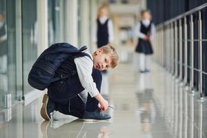 niño sentado en el suelo. niños de la escuela en uniforme juntos en el pasillo foto