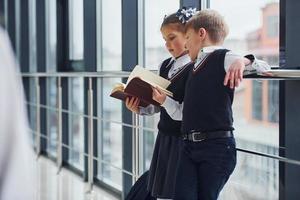 School kids in uniform reading book together in corridor. Conception of education photo