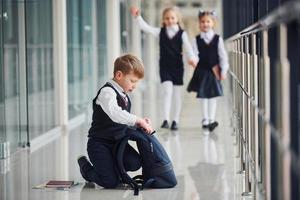 Boy sitting on the floor. School kids in uniform together in corridor photo