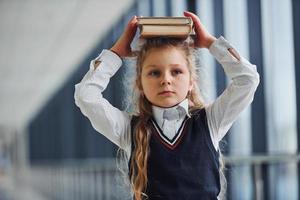 Young little school girl in uniform standing in hallway with books photo