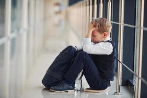 niño en uniforme sentado solo sintiéndose triste en la escuela. concepto de acoso foto