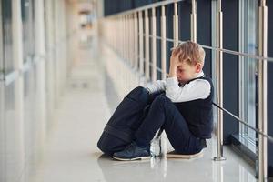 niño en uniforme sentado solo sintiéndose triste en la escuela. concepto de acoso foto