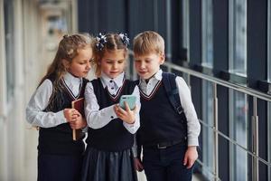 School kids in uniform together with phone in corridor. Conception of education photo