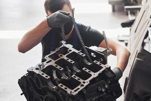 Professional repairman in black protective mask works with broken automobile engine photo