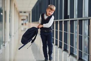 Little school boy in uniform walking in corridor with backpack photo