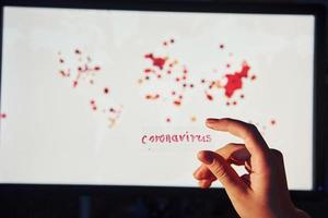 Man's hand holds lens with coronavirus title on it against background with world map of infection photo