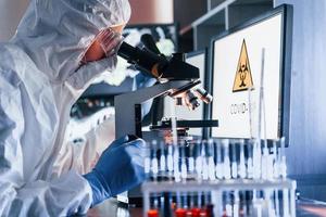 Monitors with information on the table. Scientist in white protective uniform works with coronavirus and blood tubes in laboratory photo