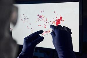 Man's hand holds lens with virus title on it against background with world map of infection photo