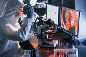 Scientist in white protective uniform near displays with data works with coronavirus and blood tubes in laboratory photo