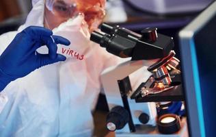 científico con ropa protectora blanca en interiores en laboratorio con lente con título de virus en él foto