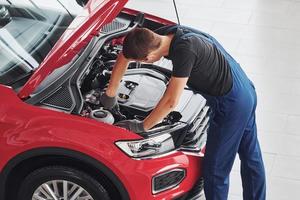 Top view of male worker in uniform that repairs red automobile photo