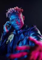 Stylish glasses and wireless headphones. Futuristic neon lighting. Young african american man in the studio photo