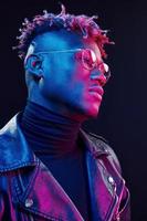 In glasses. Futuristic neon lighting. Young african american man in the studio photo