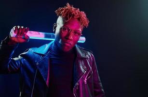 Holding lighting equipment. Futuristic neon lighting. Young african american man in glasses standing in studio photo