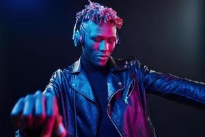 Dancing with headphones on. Futuristic neon lighting. Young african american man in the studio photo