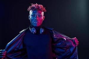 Stylish glasses and wireless headphones. Futuristic neon lighting. Young african american man in the studio photo