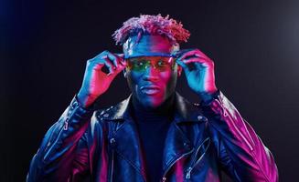 en vasos iluminación de neón futurista. joven afroamericano en el estudio foto