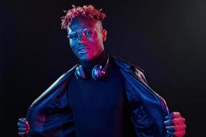 gafas elegantes y auriculares inalámbricos. iluminación de neón futurista. joven afroamericano en el estudio foto