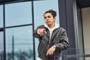 Handsome young man with curly black hair is on the street against building photo