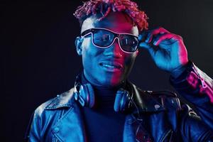 Stylish glasses and wireless headphones. Futuristic neon lighting. Young african american man in the studio photo