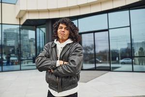 Handsome young man with curly black hair is on the street against building photo