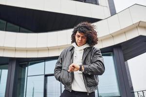 Handsome young man with curly black hair posing for the camera on the street against building photo