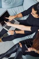 Man with curly hair and woman that in black clothes sitting with laptop indoors have a work photo