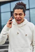 Handsome young man with curly black hair is on the street against building talking by the phone photo