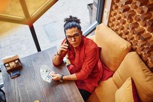 Top view of rich man in red and black clothes that sitting indoors in cafe with lot of money in hand