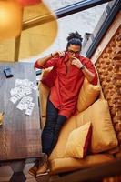 Rich man in red and black clothes sitting indoors in cafe with lot of money on the table