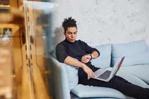 apuesto joven con cabello negro rizado en el interior con una computadora portátil foto