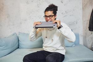 Angry young man with curly black hair goes crazy and angry with laptop in hands photo