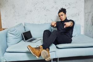 Handsome young man with curly black hair indoors with laptop have fun photo