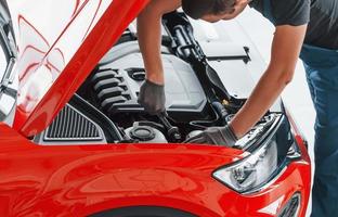 Top view of male worker in uniform that repairs red automobile photo