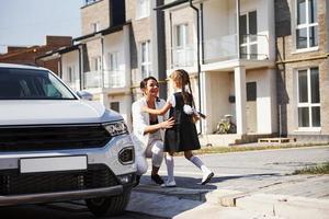 Mother with daughter in school uniform outdoors near white car photo