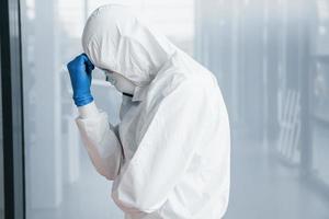 Male doctor scientist in lab coat, defensive eyewear and mask feels bad, exhausted and sick photo