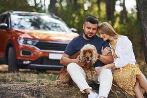 Couple with dog have weekend outdoors in the forest with car behind them photo